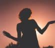silhouette of woman raising her hands during sunset